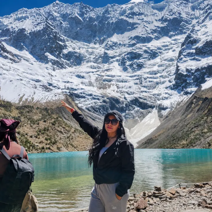 Solo traveler standing beside Humantay Lake beneath snowy mountains.