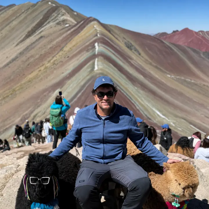 Traveler seated between two alpacas at Vinicunca in Peru.