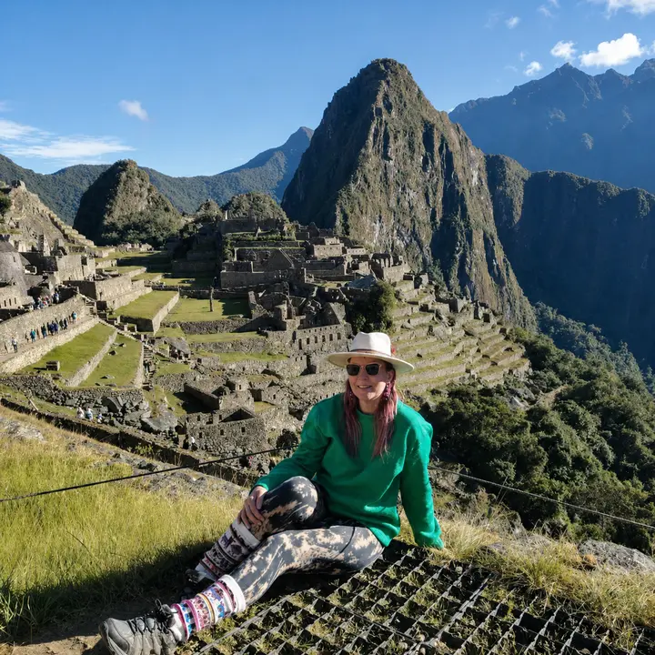 Traveler in a green sweater seated above the Machu Picchu citadel