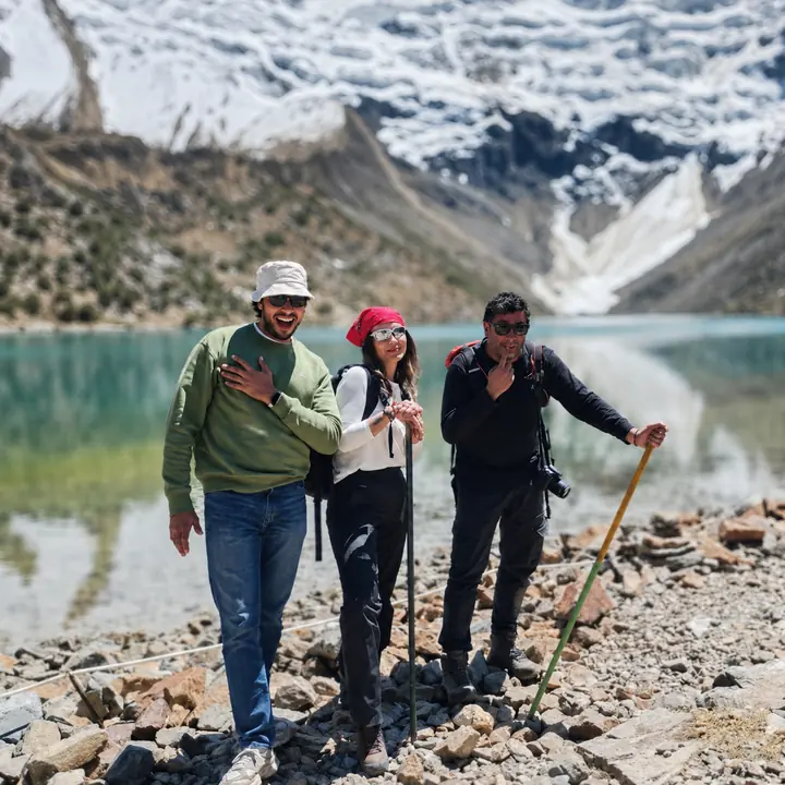 Three travelers posing beside Humantay Lake beneath snowy Andean peaks.
