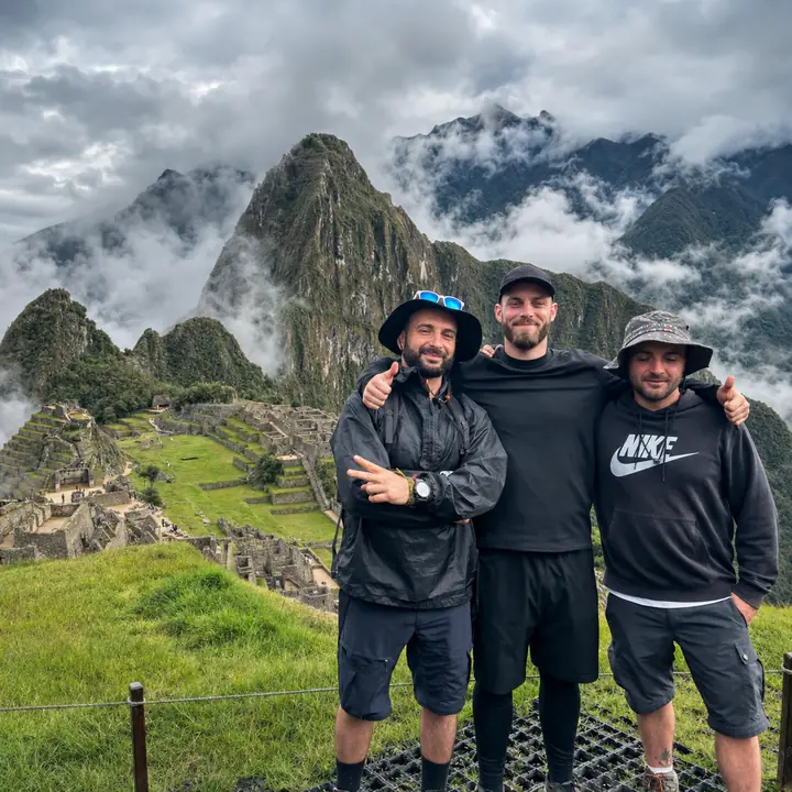 Three travelers at Machu Picchu surrounded by Andean clouds.