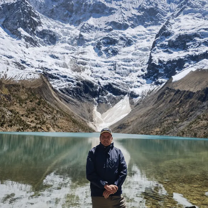 Traveler posing before Humantay Lake and the snow-covered Andes.