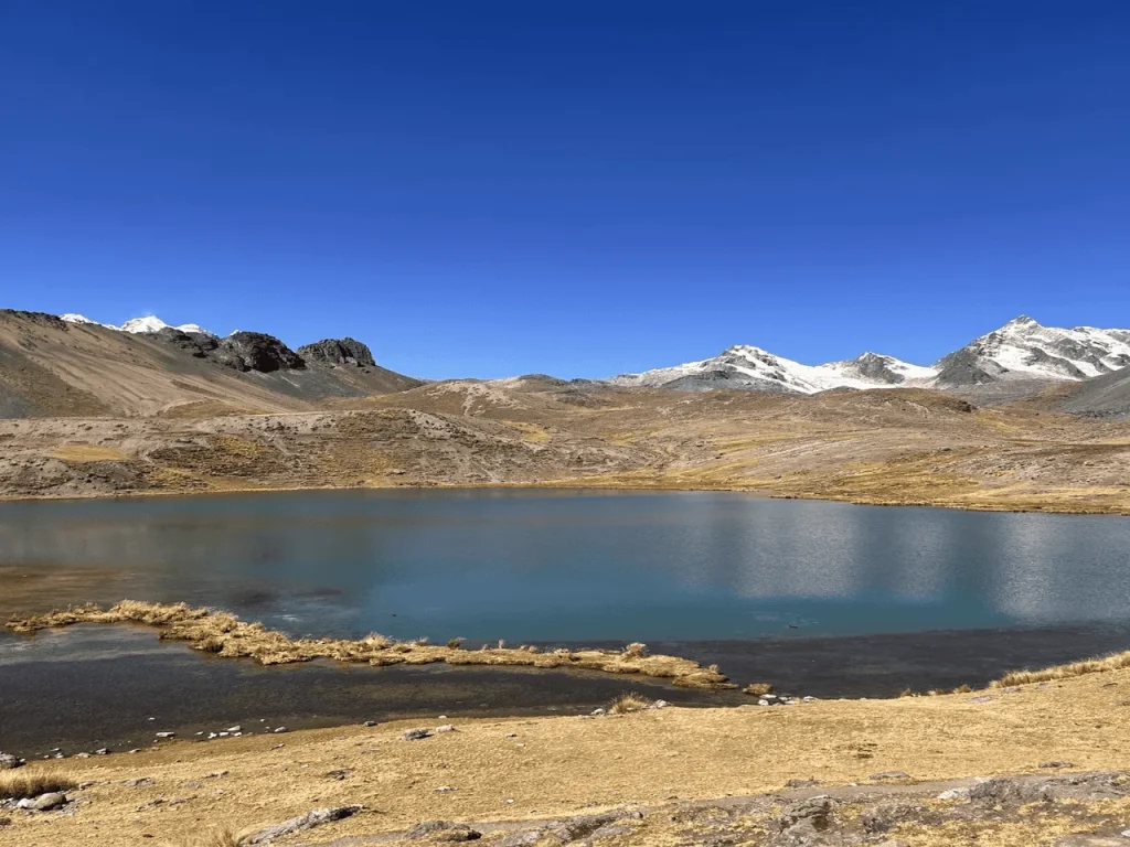 Wide Andean lake with snow-capped Ausangate mountains in the background near Cusco