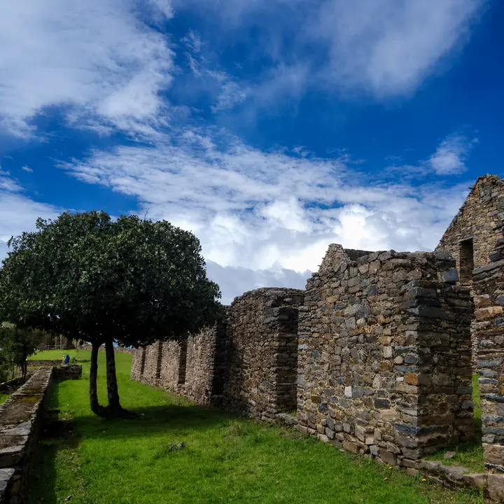 Choquequirao stone ruins and green lawns beneath a dramatic mountain sky.