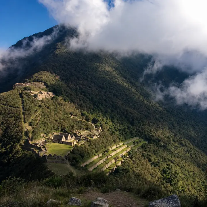 Panoramic view of Choquequirao ruins surrounded by cloud-covered mountains.