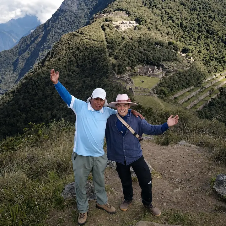 Two travelers celebrating with a panoramic view of Choquequirao behind them.